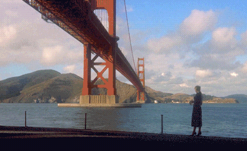 A shot from Hitchcock's Vertigo showing the lovely Kim Novak under the Golden Gate Bridge on a beautiful partly cloudy day, throwing flowers into the bay.
