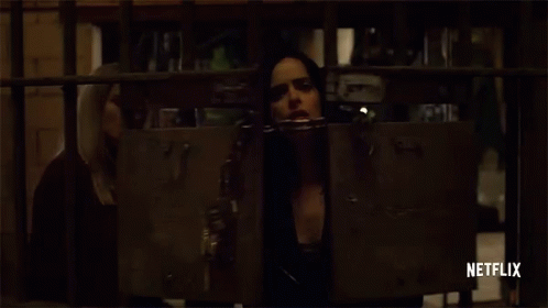 Jessica Jones breaks a chain with padlock to open a gate, dramatically